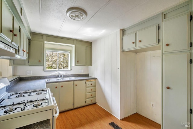 kitchen featuring visible vents, a sink, white gas stove, green cabinets, and light wood-style flooring