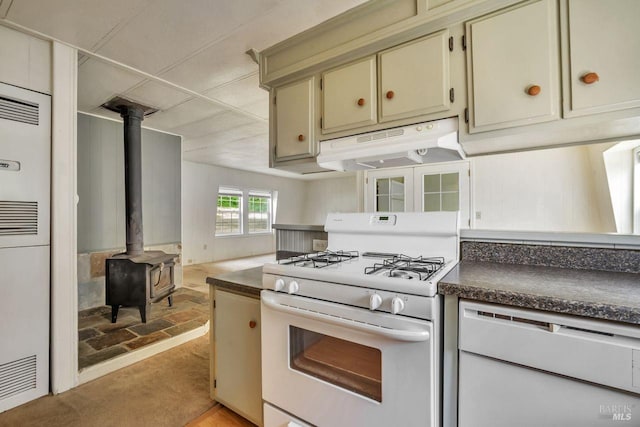 kitchen with dark countertops, white range with gas cooktop, cream cabinetry, under cabinet range hood, and a wood stove