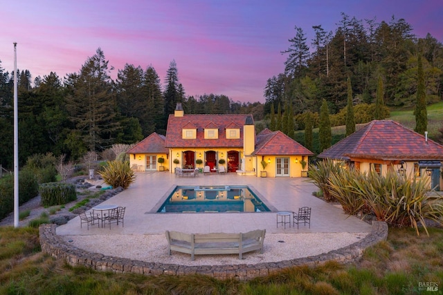 rear view of property with an outdoor pool, a patio, a chimney, and stucco siding