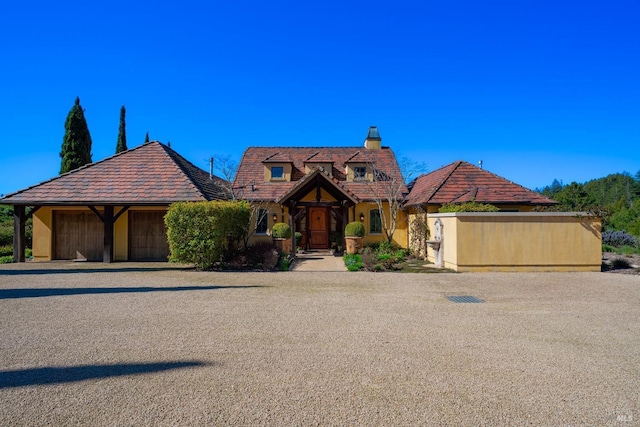 view of front facade with a detached garage, a tile roof, stucco siding, and a chimney
