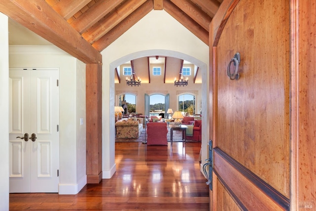 corridor featuring baseboards, arched walkways, hardwood / wood-style flooring, beam ceiling, and high vaulted ceiling