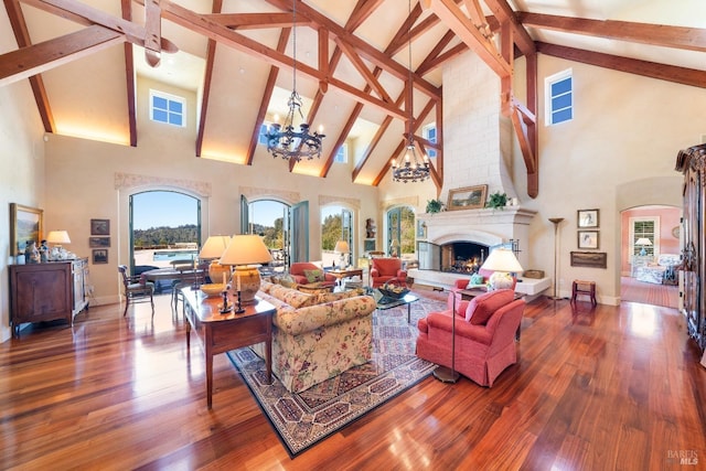 living room with an inviting chandelier, a fireplace, beamed ceiling, arched walkways, and wood finished floors