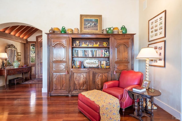 sitting room with arched walkways, wood finished floors, baseboards, and vaulted ceiling with beams