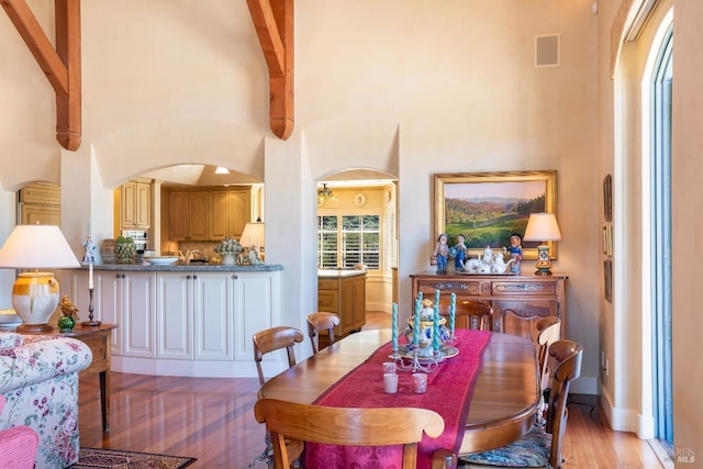 dining room with arched walkways, visible vents, a high ceiling, light wood finished floors, and baseboards