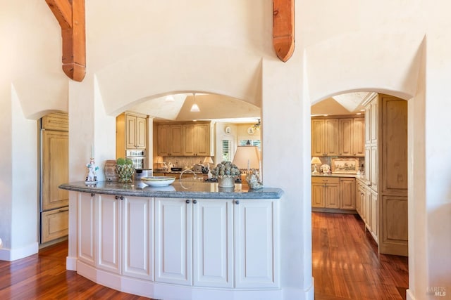 kitchen with tasteful backsplash, arched walkways, wood finished floors, and a peninsula