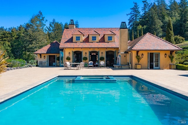 rear view of property featuring a patio area, a pool with connected hot tub, stucco siding, and a chimney