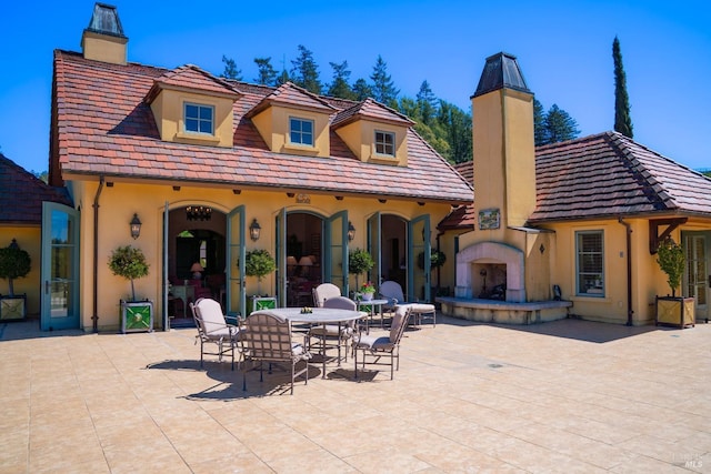 back of property featuring a patio, a chimney, stucco siding, and exterior fireplace