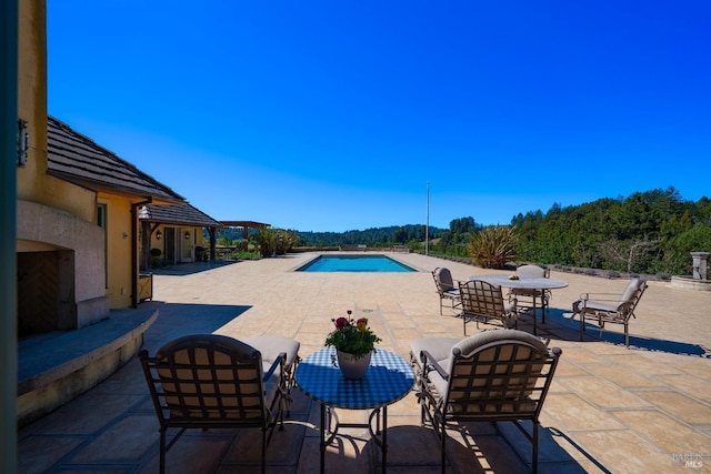 outdoor pool featuring outdoor dining space, a patio area, and a view of trees