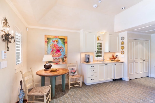kitchen featuring baseboards, a sink, light countertops, crown molding, and white cabinetry