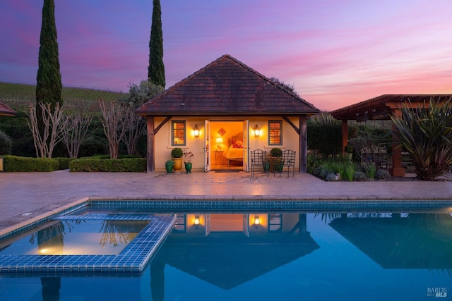 pool at dusk with a storage structure, an outbuilding, a patio area, and a pool with connected hot tub