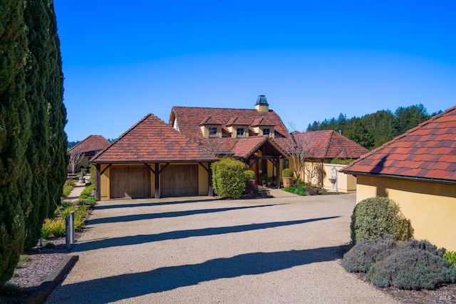 view of front of house featuring stucco siding, a chimney, driveway, a garage, and a tiled roof