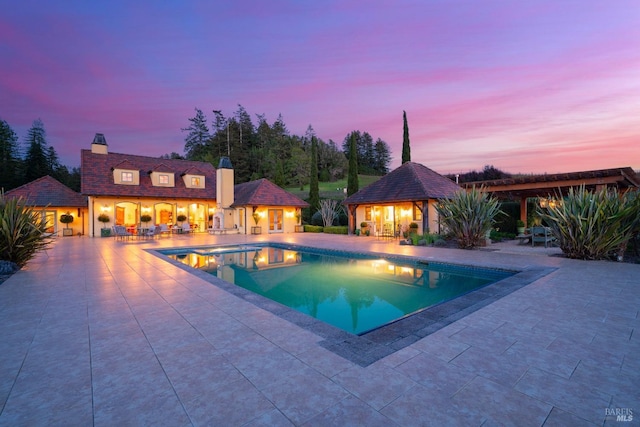 pool at dusk with an outdoor structure, an outdoor pool, an exterior structure, a patio area, and a jacuzzi