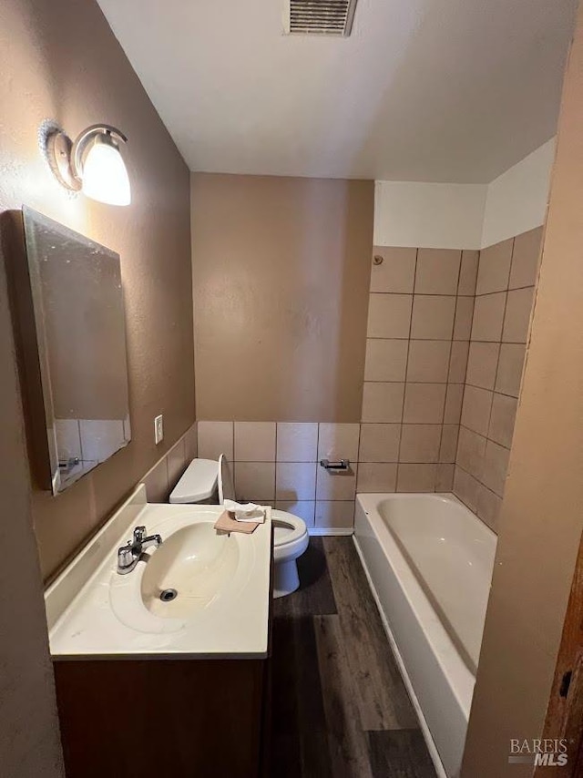 bathroom featuring visible vents, tile walls, wood finished floors, vanity, and toilet