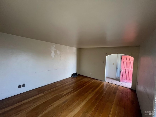 spare room featuring arched walkways, hardwood / wood-style floors, and visible vents
