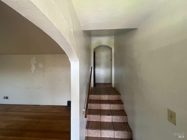 stairway featuring visible vents, arched walkways, and wood finished floors