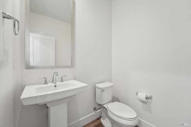 bathroom with toilet, wood finished floors, a sink, and baseboards
