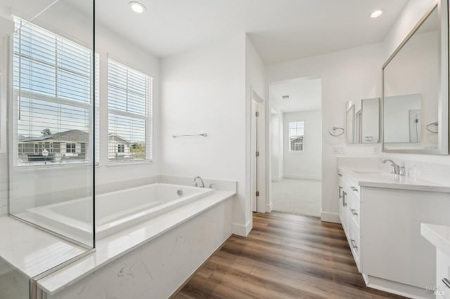 bathroom with baseboards, recessed lighting, vanity, wood finished floors, and a garden tub