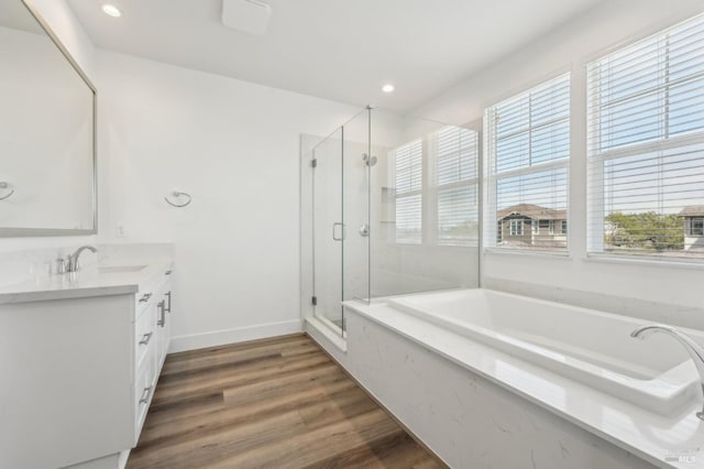 bathroom with a bath, a sink, double vanity, wood finished floors, and a stall shower