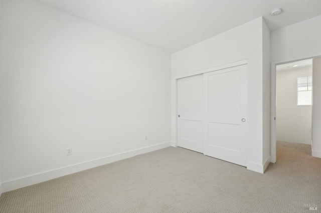 unfurnished bedroom with light carpet, a closet, and baseboards