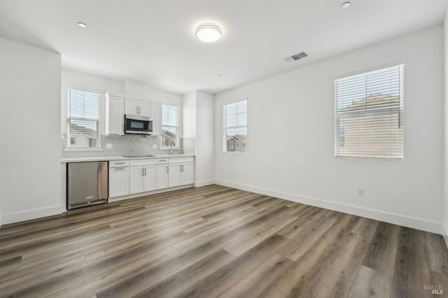 kitchen with tasteful backsplash, visible vents, stainless steel microwave, white cabinetry, and wood finished floors