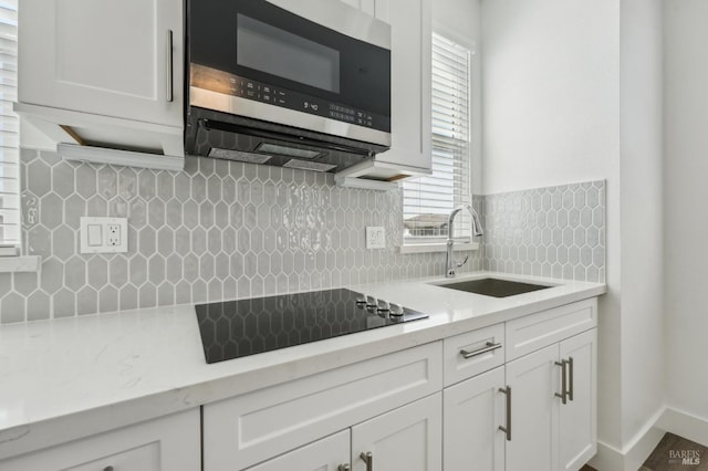 kitchen featuring tasteful backsplash, black electric cooktop, a sink, stainless steel microwave, and white cabinetry