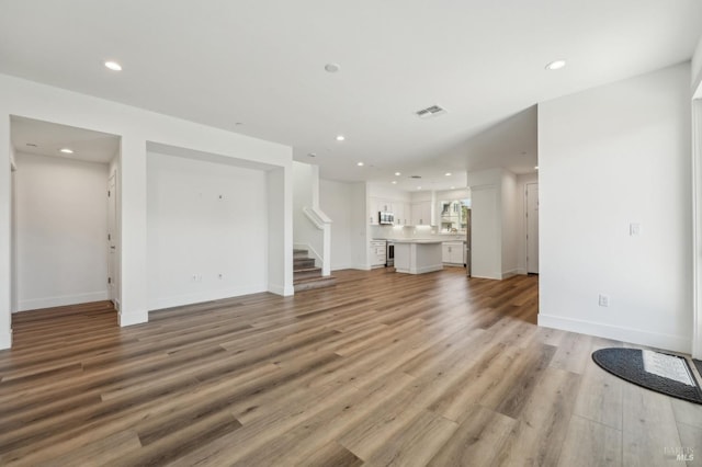 unfurnished living room with light wood-style floors, recessed lighting, visible vents, and stairs