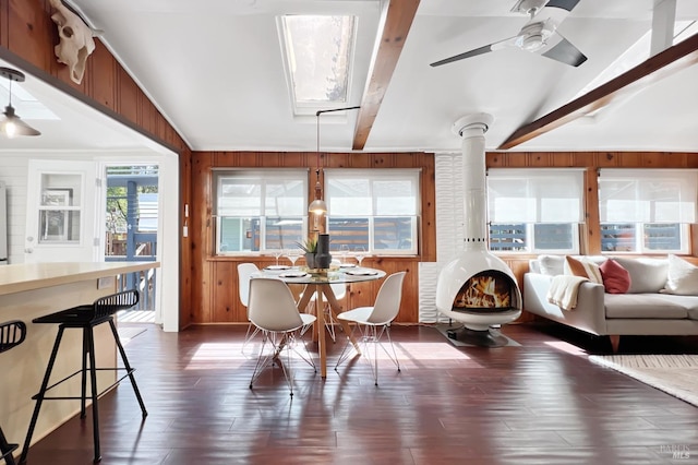 dining room with wood walls, ceiling fan, and vaulted ceiling with beams