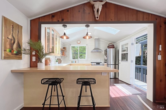 kitchen with stainless steel appliances, dark wood-type flooring, wall chimney exhaust hood, and lofted ceiling with skylight