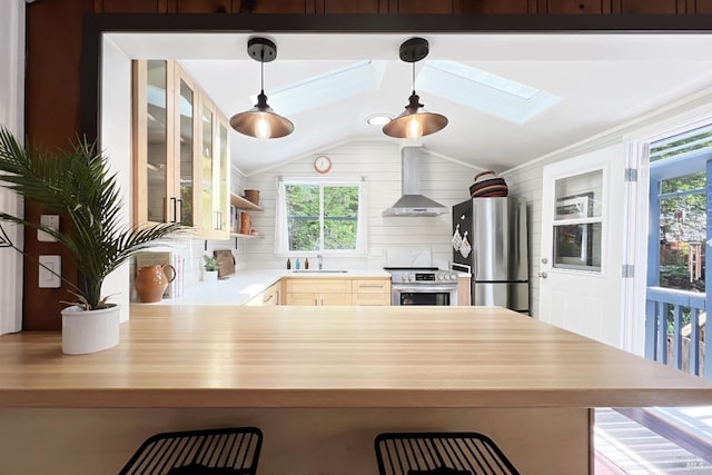 kitchen with vaulted ceiling with skylight, a peninsula, wall chimney exhaust hood, a breakfast bar area, and stainless steel appliances
