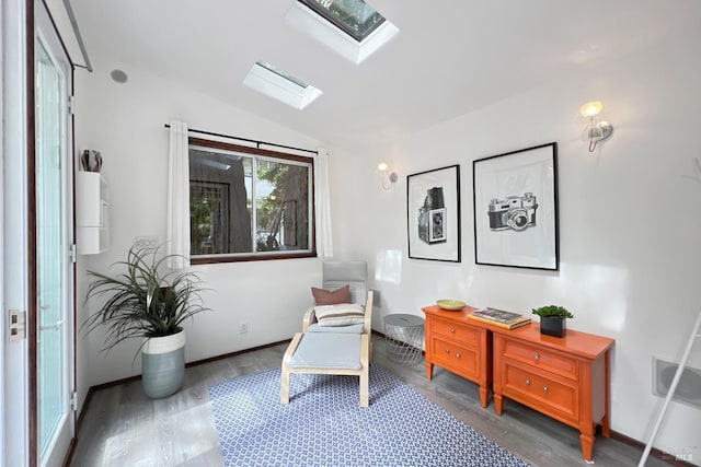 sitting room featuring vaulted ceiling with skylight, baseboards, and wood finished floors