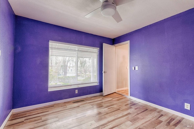 unfurnished room featuring wood finished floors, a textured wall, baseboards, and a ceiling fan