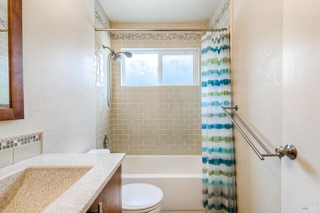 bathroom with toilet, shower / bathtub combination with curtain, vanity, and a textured wall