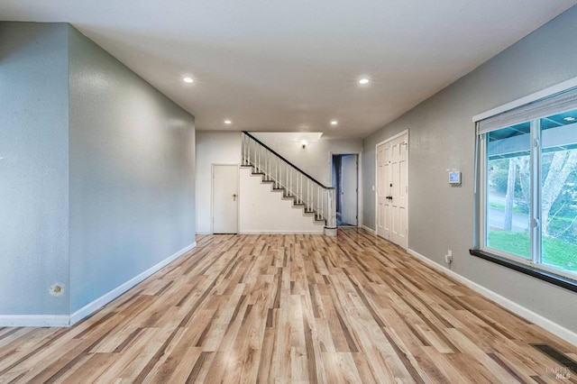 unfurnished living room featuring recessed lighting, stairs, light wood-style floors, and baseboards