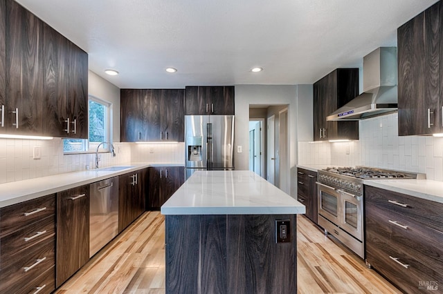 kitchen featuring appliances with stainless steel finishes, light wood-type flooring, wall chimney range hood, decorative backsplash, and a sink