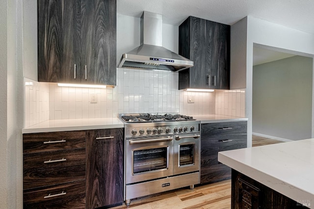 kitchen with modern cabinets, decorative backsplash, wall chimney exhaust hood, and range with two ovens