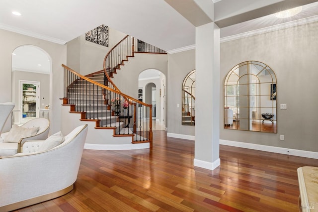 entryway with crown molding, arched walkways, wood finished floors, stairs, and baseboards