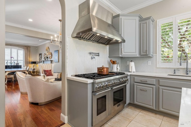kitchen with wall chimney range hood, double oven range, gray cabinets, a sink, and light countertops