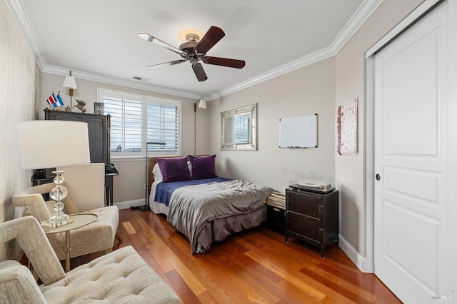 bedroom with ceiling fan, ornamental molding, visible vents, baseboards, and hardwood / wood-style flooring