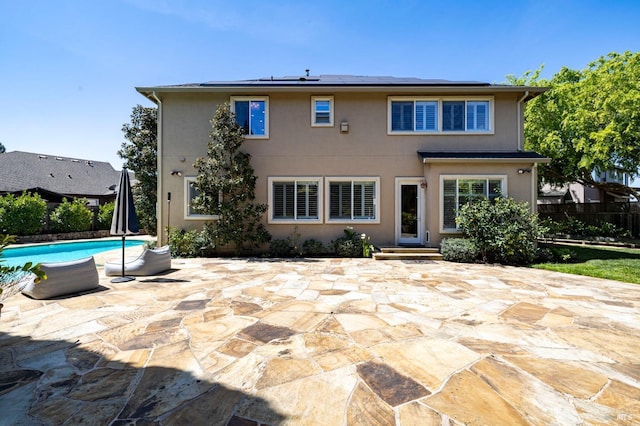rear view of property with fence, roof mounted solar panels, a patio, and stucco siding