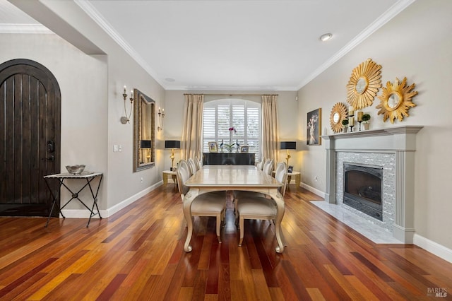 dining space with baseboards, crown molding, a fireplace with flush hearth, arched walkways, and wood finished floors