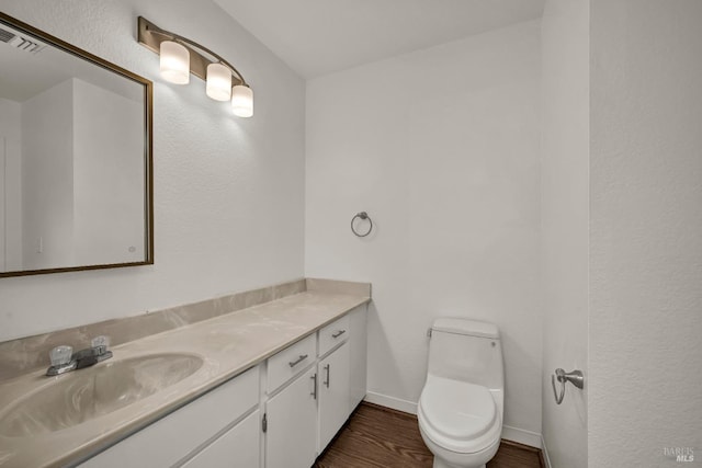 half bathroom featuring visible vents, baseboards, toilet, vanity, and wood finished floors