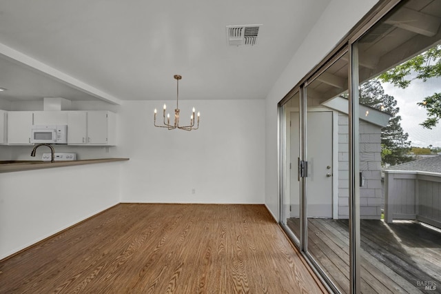unfurnished dining area featuring wood finished floors, a notable chandelier, visible vents, and a wealth of natural light