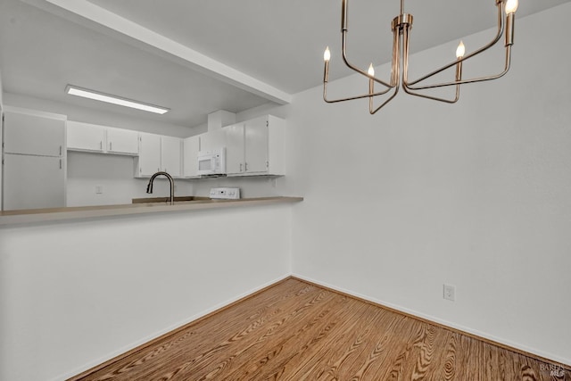 kitchen with an inviting chandelier, light countertops, white microwave, white cabinetry, and wood finished floors