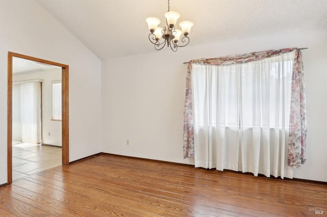 empty room with baseboards, vaulted ceiling, an inviting chandelier, and hardwood / wood-style flooring