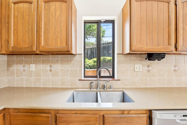 kitchen featuring a sink, backsplash, white dishwasher, and light countertops
