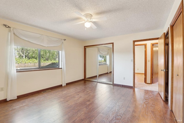 unfurnished bedroom with a ceiling fan, a textured ceiling, visible vents, wood finished floors, and baseboards