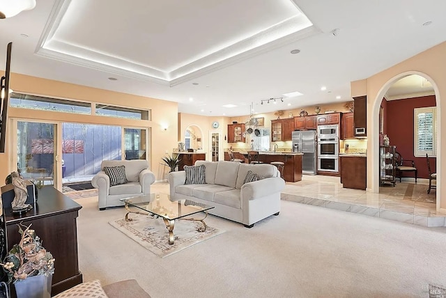 living room featuring a wealth of natural light, arched walkways, light colored carpet, and a raised ceiling