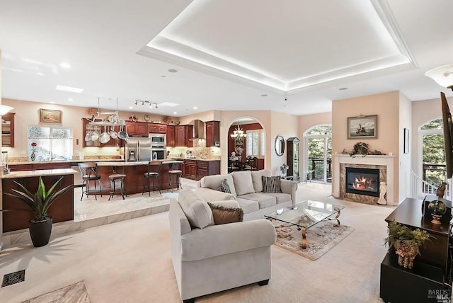 living area with a chandelier, a tray ceiling, arched walkways, and light colored carpet