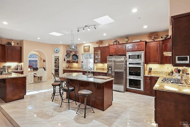 kitchen with light stone countertops, a skylight, a kitchen bar, and appliances with stainless steel finishes
