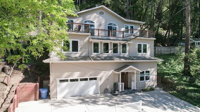 view of front of property featuring an attached garage, driveway, fence, and a balcony